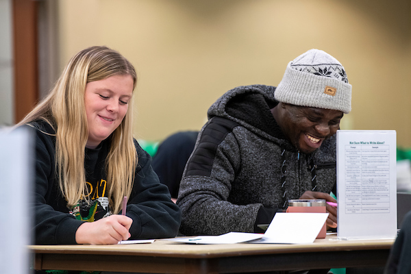 a White woman and Black man writing cards to new students
